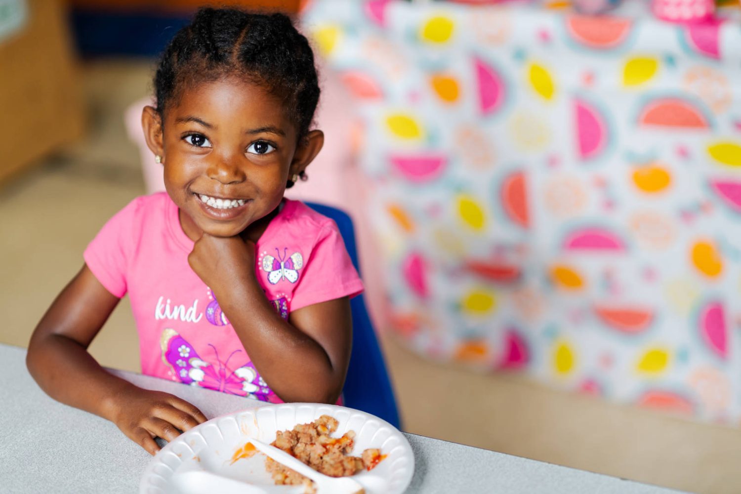 A young girl with a plate of food smiles at the camera